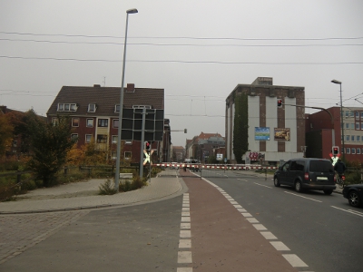 Farbfoto: Eine geschossene Eisenbahnschranke über der Nesserlander Straße in Emden im Oktober des Jahres 2012. Vor der Eisenbahnstrecke Leer-Emden biegt vorne im Bild die Küstenbahnstraße von der Nesserlander Straße nach links ab. Hinter der geschlossenen Bahnschranke biegt links die Fürbringerstraße von der Nesserlander Straße ab. Rechts hinter der geschlossenen Schranke ein Hochbunker aus dem Zweiten Weltkrieg. Foto: Erwin Thomasius. 